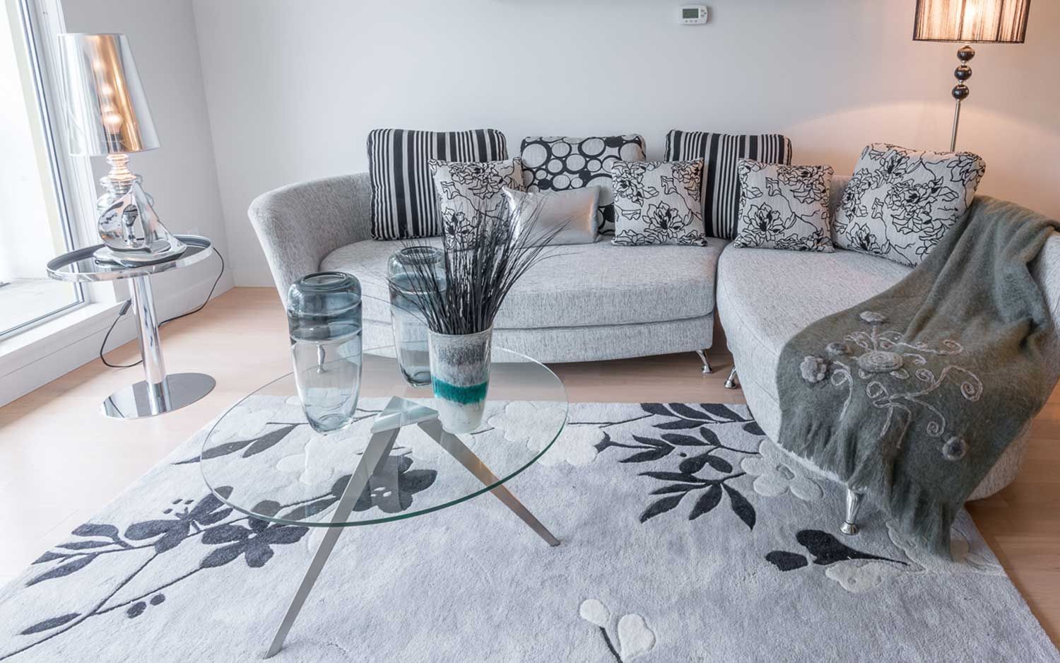 Living room with a white sofa, patterned pillows, glass coffee table, and floral rug.