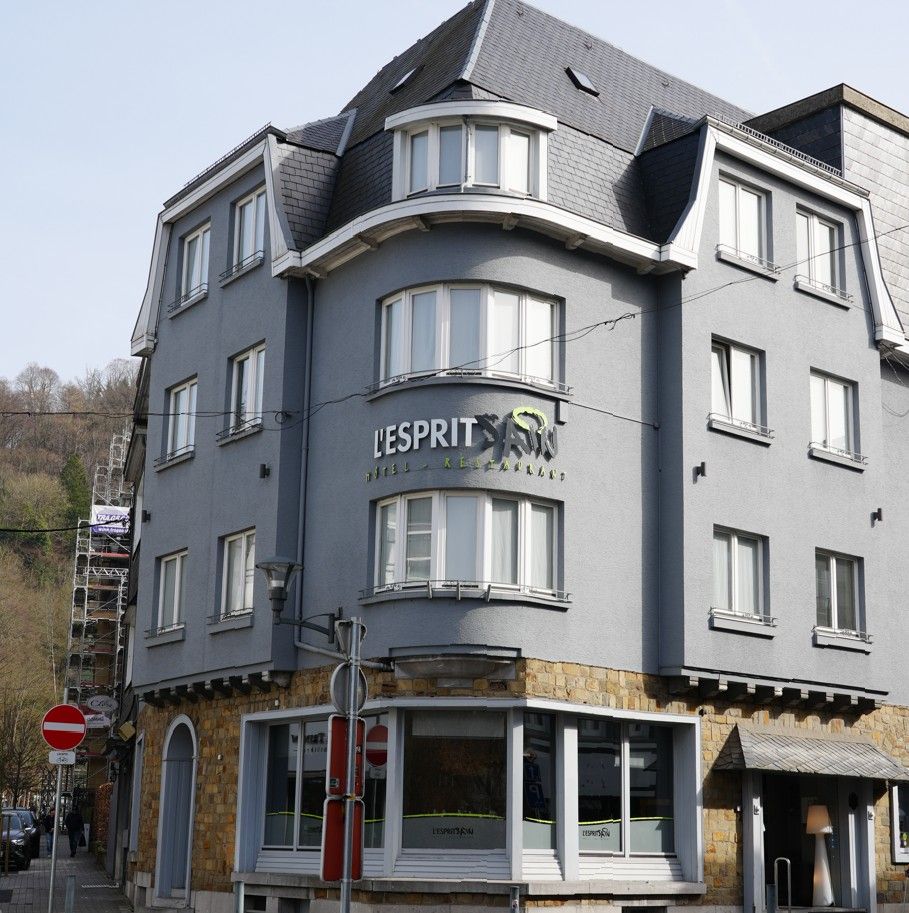 Een grijs, meerlaags gebouw op een hoek met een stenen sokkel en het opschrift