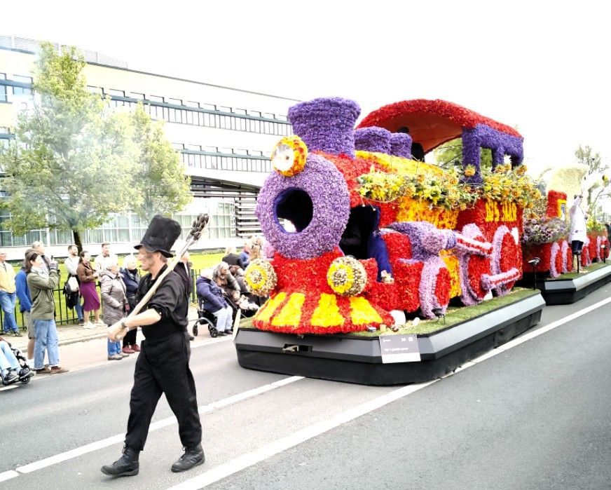 Een kleurrijke, met bloemen bedekte praalwagen met een cartoongezicht, aangevoerd door een deelnemer.