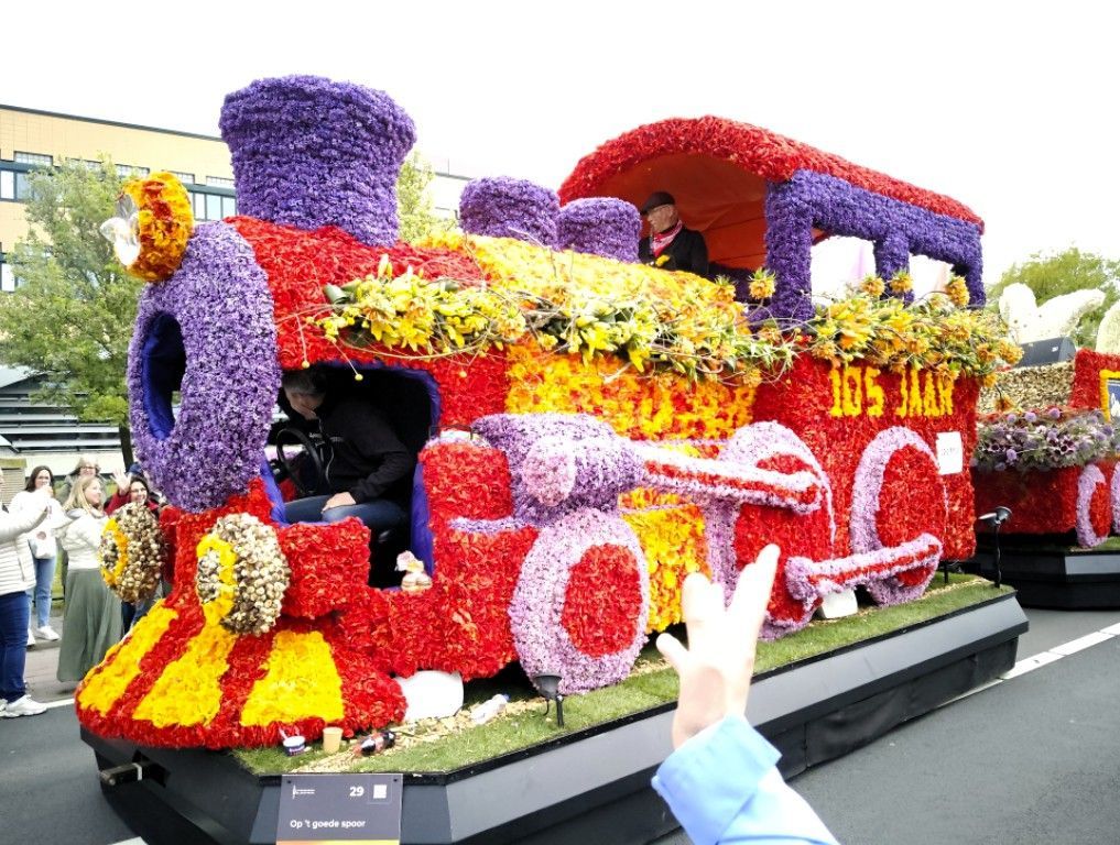 Een met bloemen bedekte rode praalwagen met paarse en gele bloemdetails in een parade.