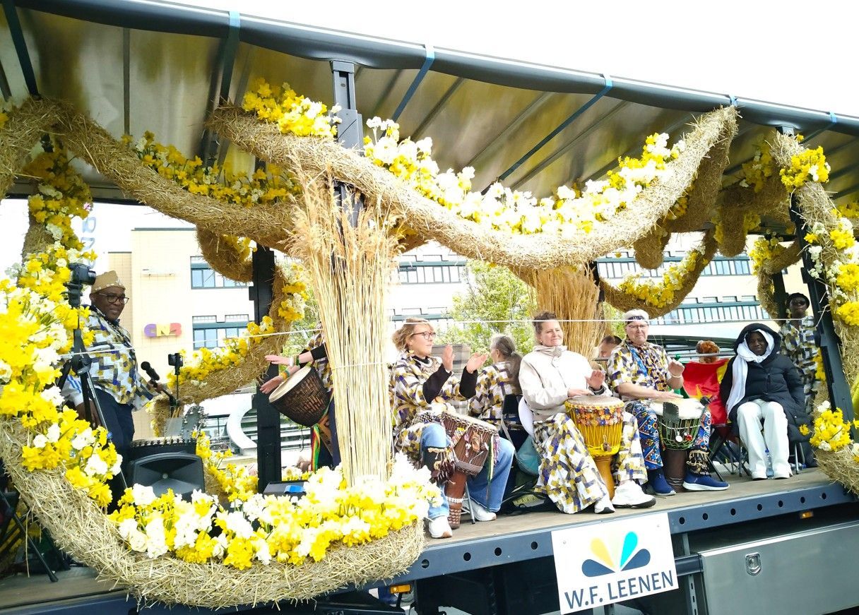 Paradewagen met gele en witte bloemen en zittende artiesten onder een afdak.