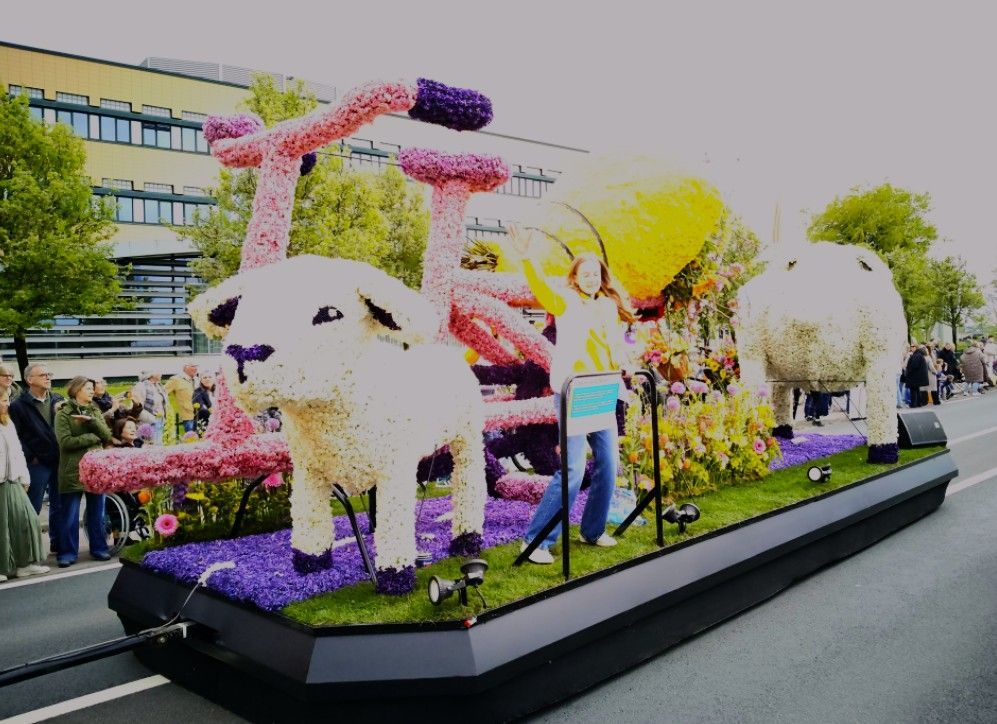 Een kleurrijke praalwagen met grote witte dierenfiguren en mensen die er buiten naast lopen.