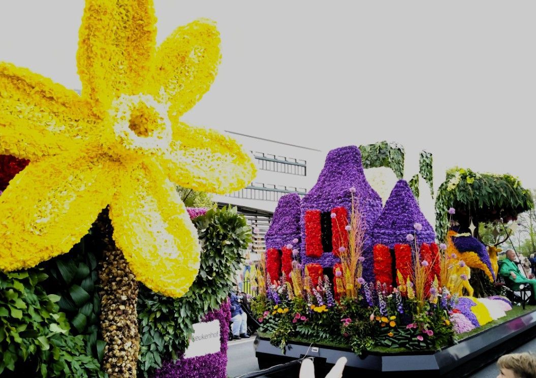 Een sculptuur van gele bloemen naast een kleurrijk, huisvormig bloemstuk in een tuinscène.