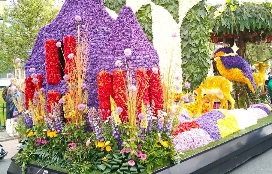 Een kleurrijke bloemenpraalwagen met hoge rode, paarse en gele bloemsculpturen in een tuindecoratie.