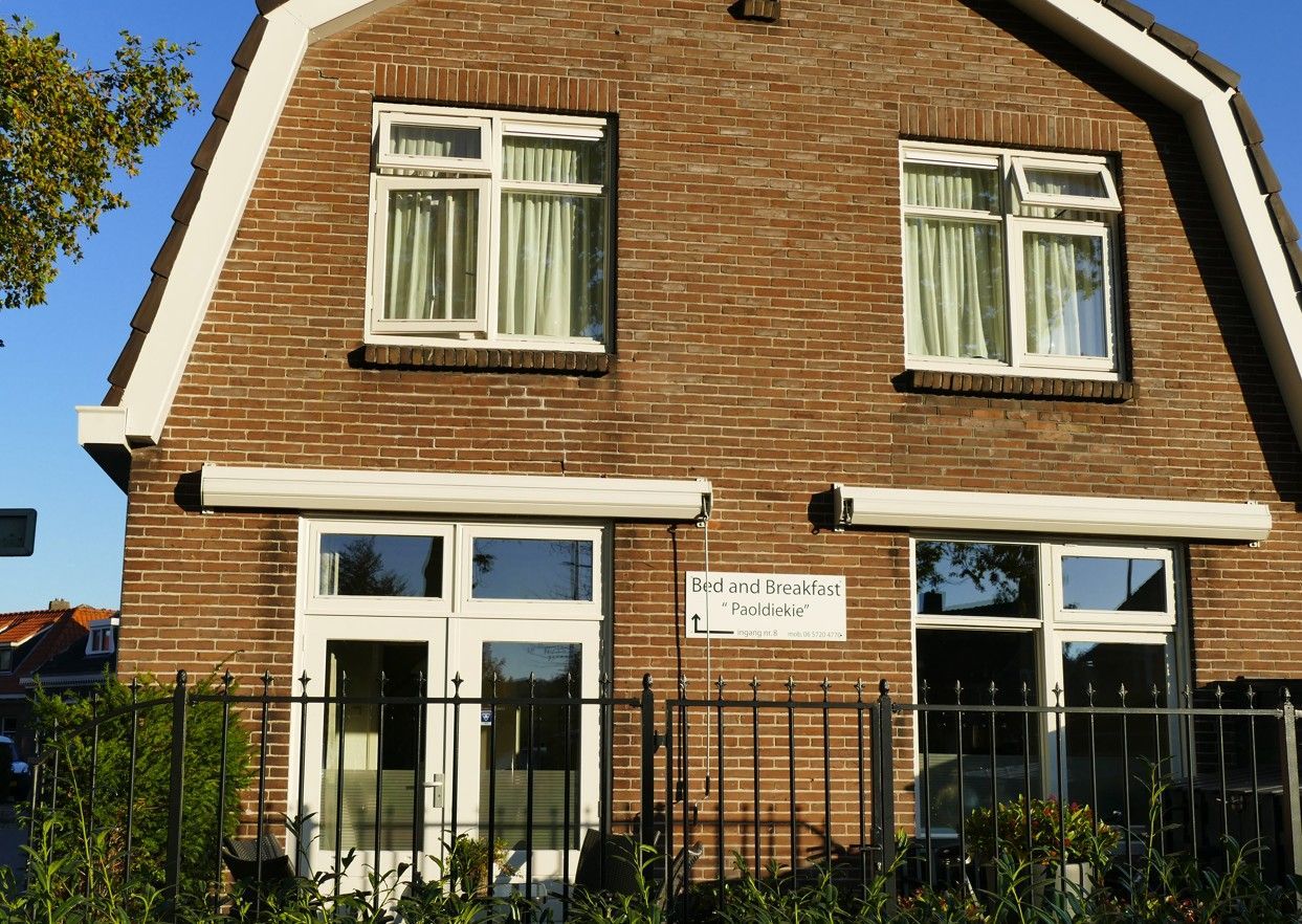 Een twee verdiepingen tellend huis van bruine baksteen met een mansardedak, en een zwart metalen hek ervoor.