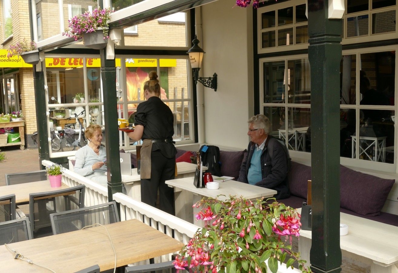 Terras van een café met een ober die twee klanten bedient die aan een tafel zitten.