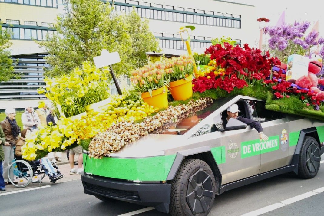 Een versierde paradeauto, bedekt met kleurrijke potplanten, rijdt door een stadsstraat.