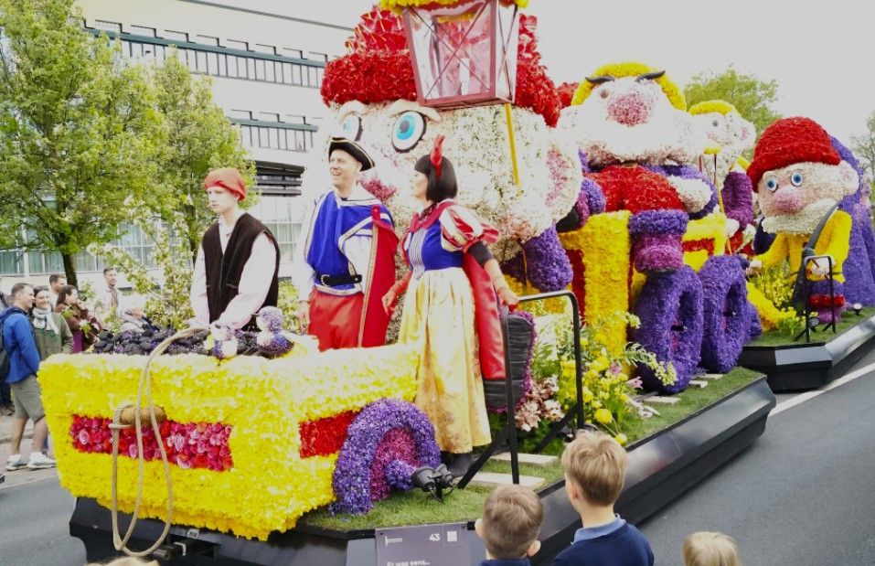 Een kleurrijke, met bloemen bedekte praalwagen met grote figuren en toeschouwers langs de route.