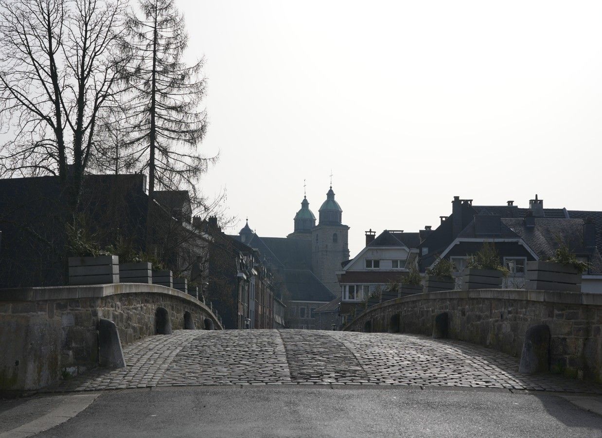 Een stenen brug leidt naar een stadje met een opvallende koepelkerk tegen een heldere hemel.