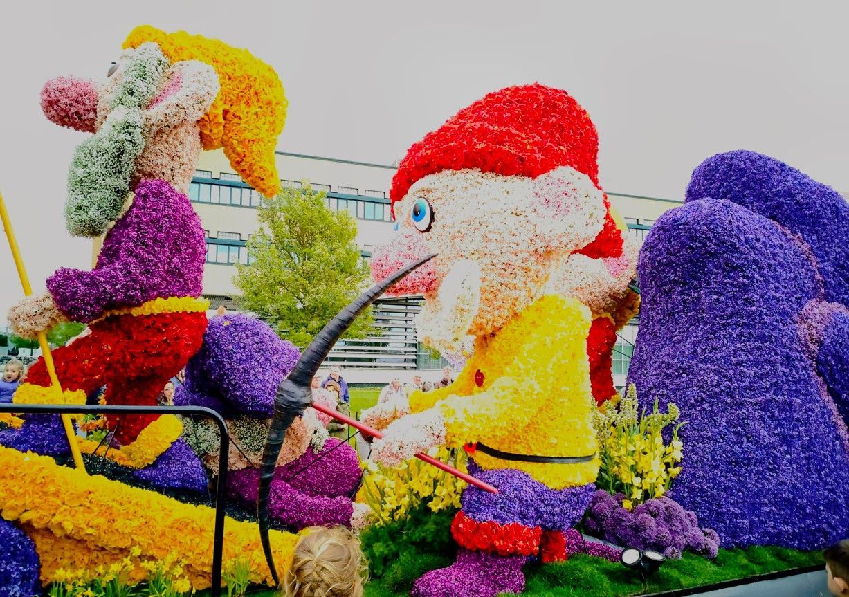 Kleurrijke bloemsculpturen van stripfiguren in een tuindecoratie met een gebouw op de achtergrond.