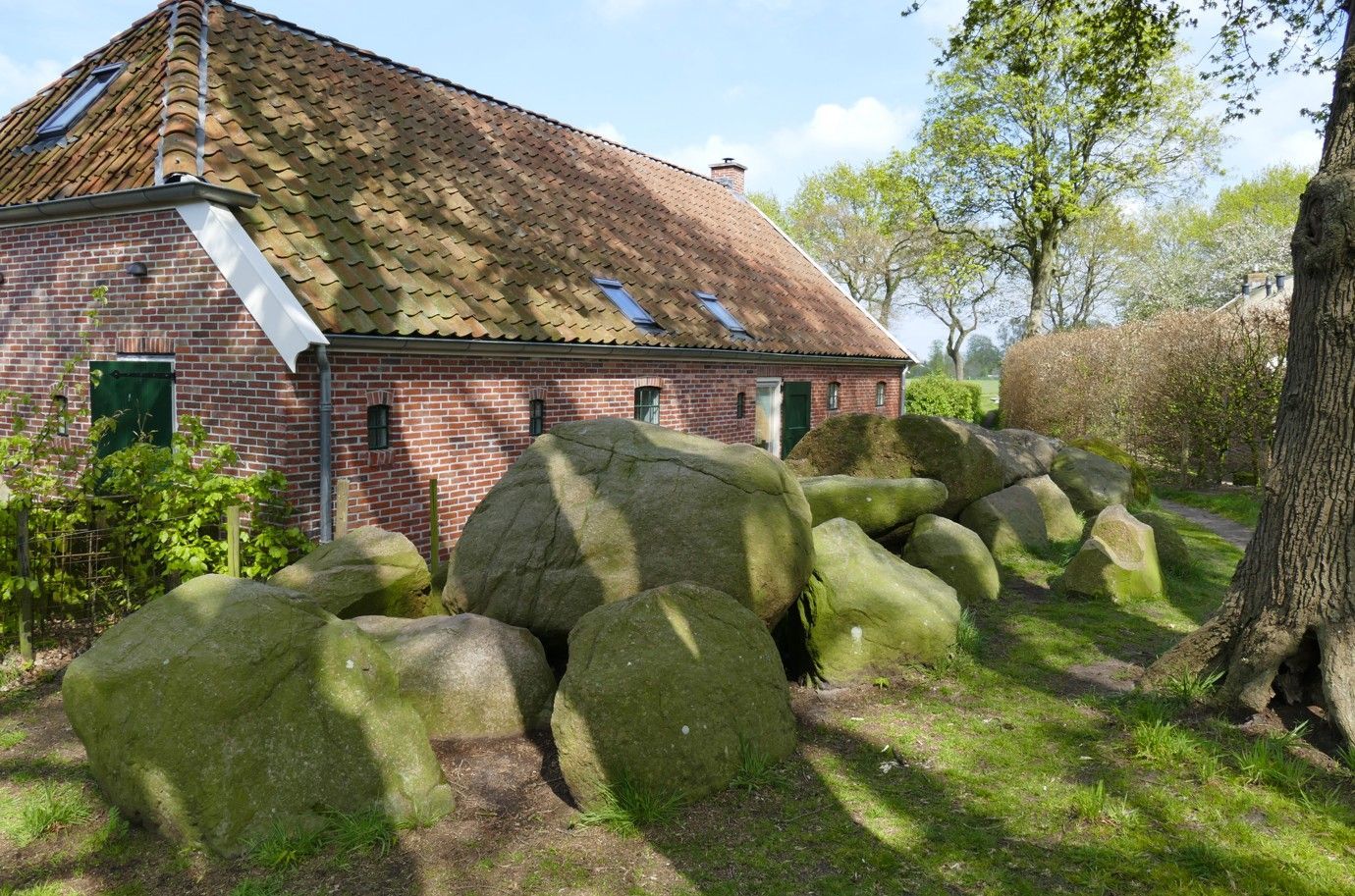 Stenen muur voor een bakstenen gebouw met een pannendak. Zonnige dag, groen gras.