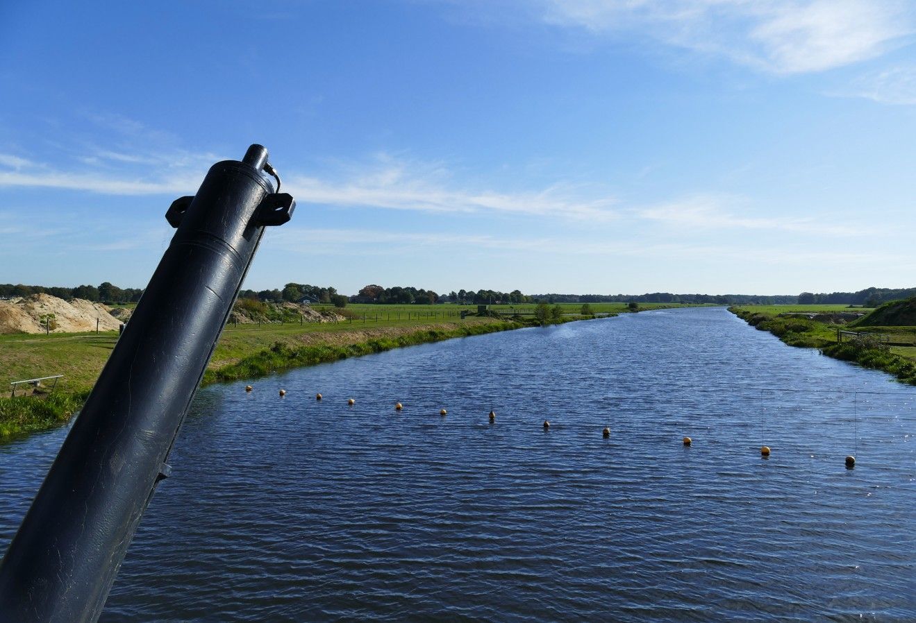 Uitzicht op een kalme, blauwe Vecht die zich door groene, open velden slingert onder een zonnige hemel.