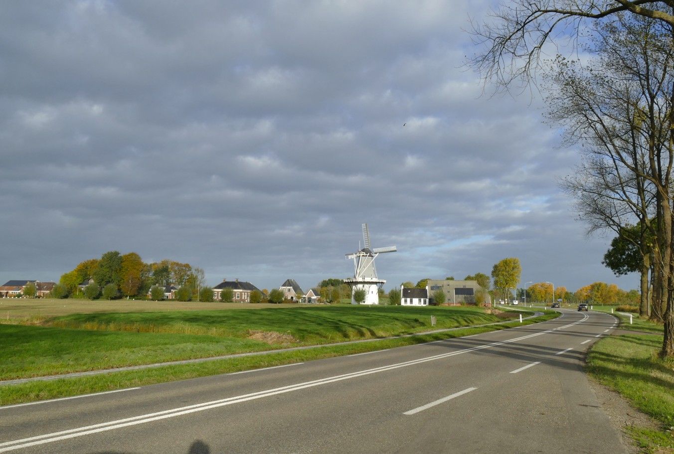Uitzicht vanaf de weg op een witte windmolen in de verte onder een bewolkte hemel.
