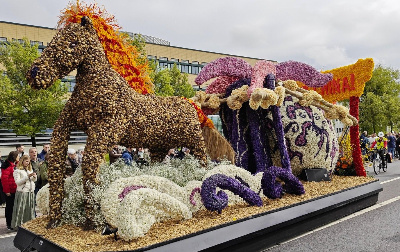 Een met bloemen bedekte paardenkoets, versierd met paarse, witte en oranje bloemdecoraties, staat buiten opgesteld.