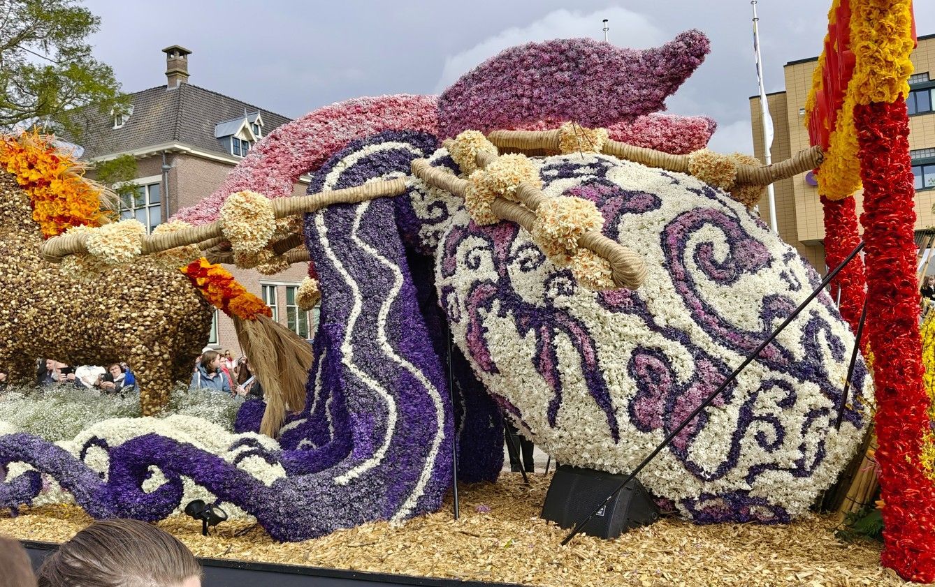 Kleurrijke praalwagen met bloemen en grote paarse, crèmekleurige en rode versieringen buiten.