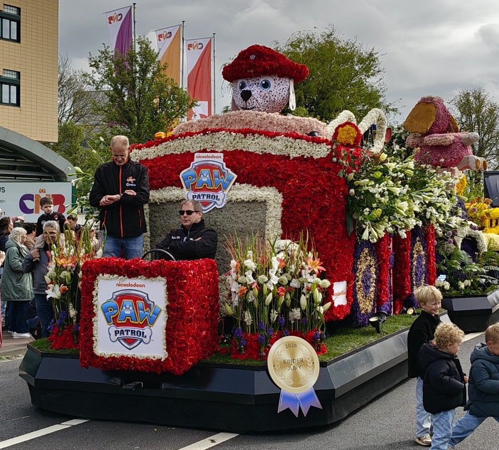 Een met bloemen bedekte praalwagen van PAW Patrol, met toeschouwers op straat.