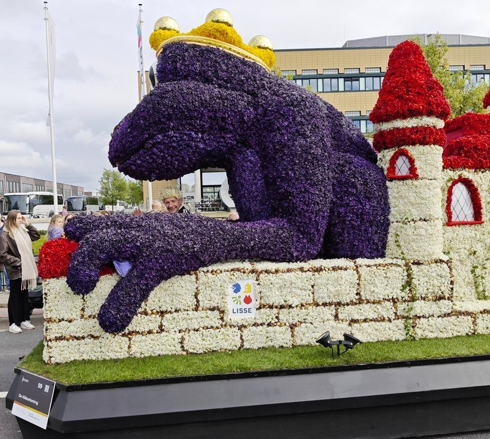 Paarse bloemensculptuur van een zittende draak naast een rood-wit kasteel in de buitenlucht.