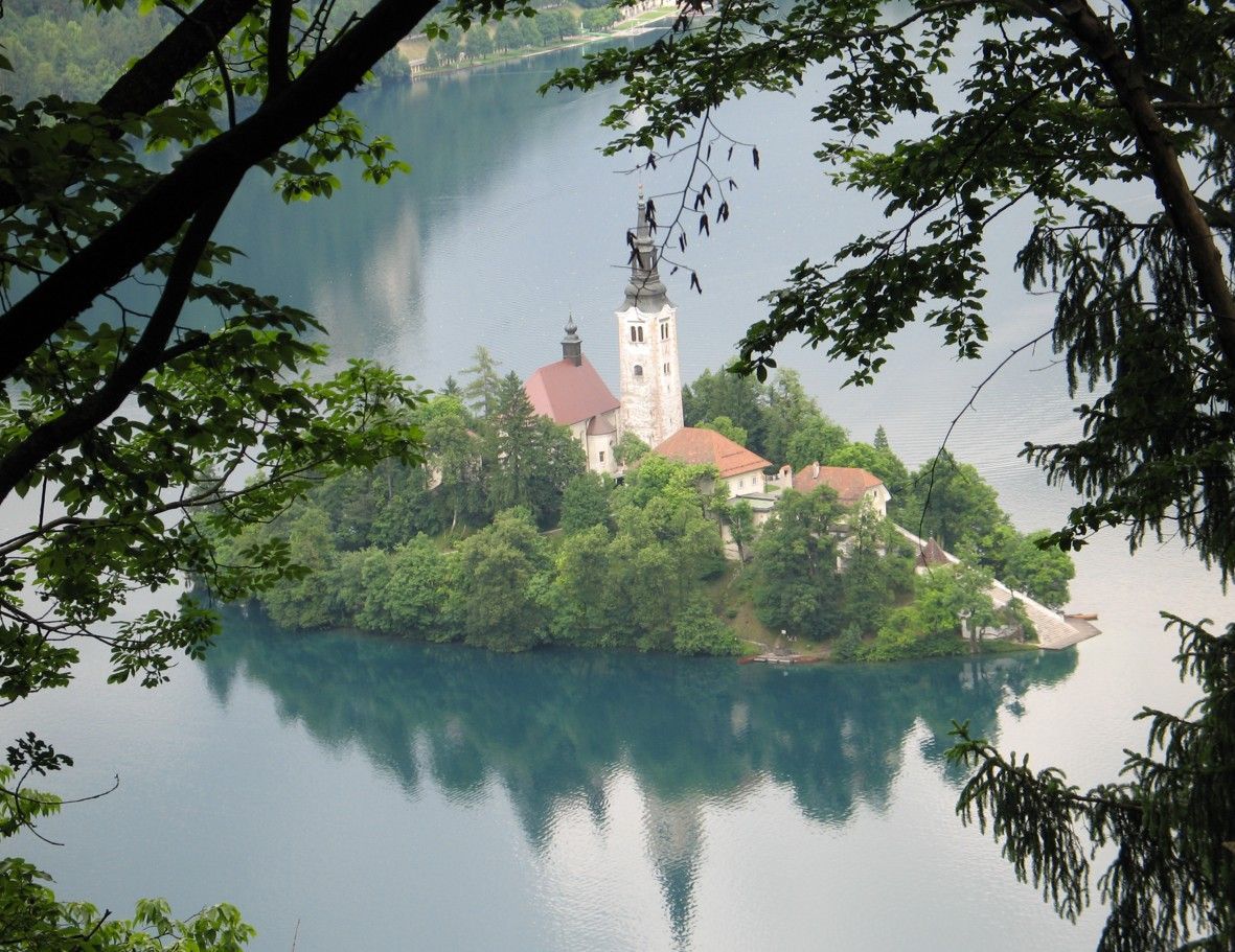 Het meer van Bled met een kerk op een eiland, omgeven door groene bomen, met weerspiegelingen in het water.