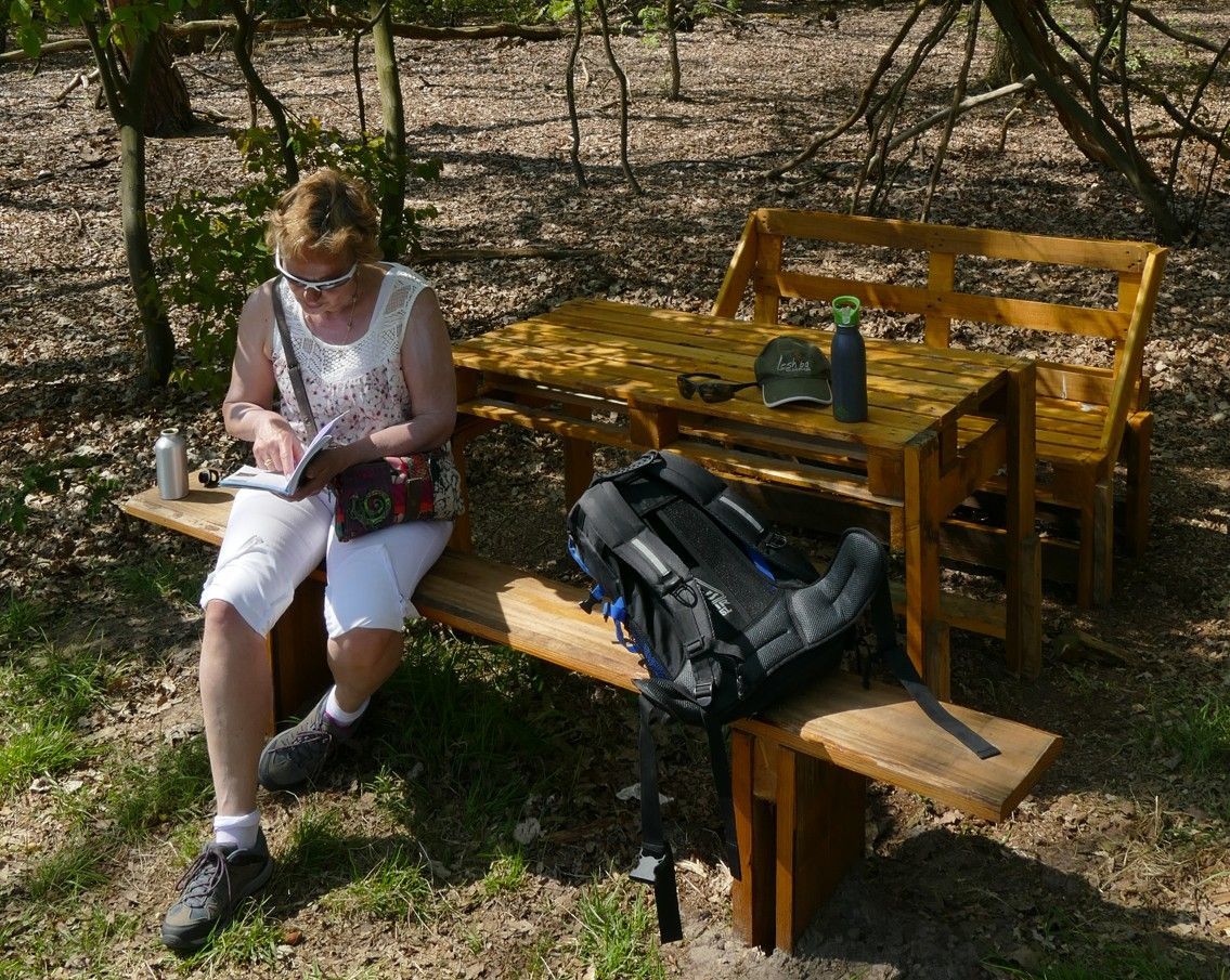 Pauze bij een houten picknicktafel in een bos en schrijft in een notitieboekje. Mijn rugzak en uitrusting liggen in de buurt.