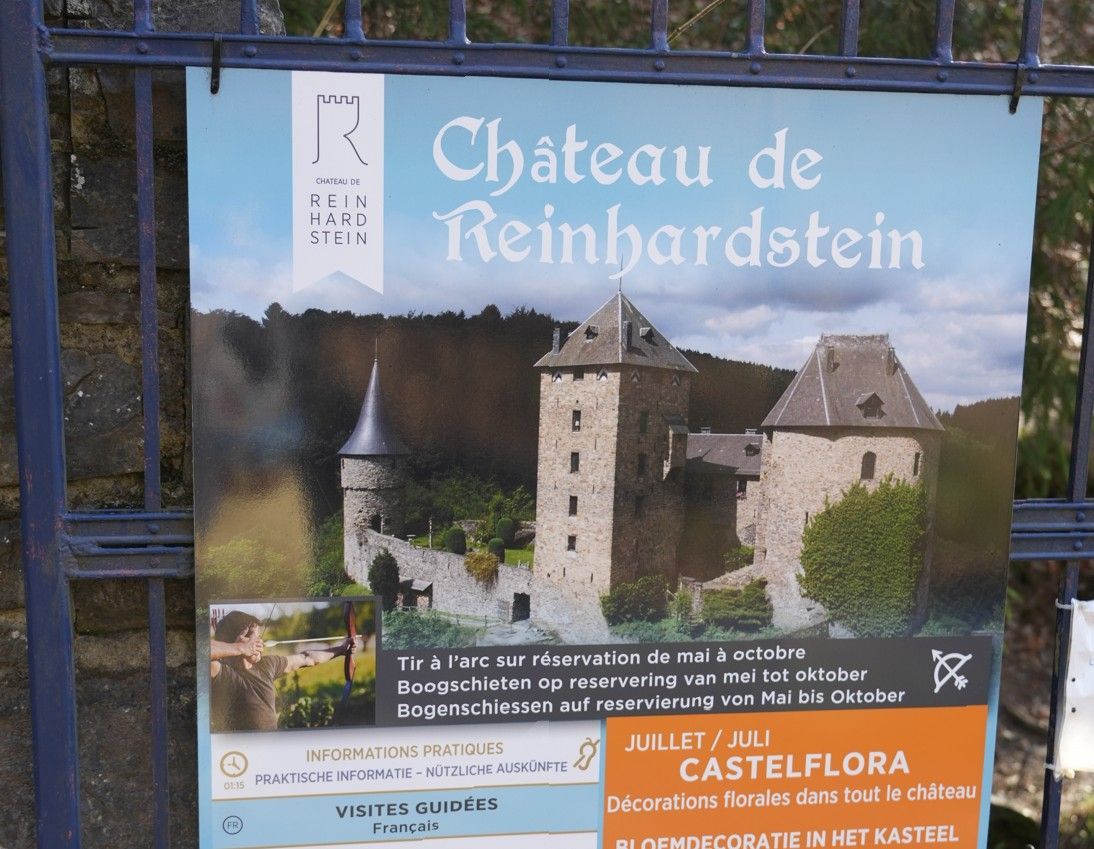 Een bord voor Château de Reinhardstein met een foto van het stenen kasteel tegen een wazige, beboste achtergrond.