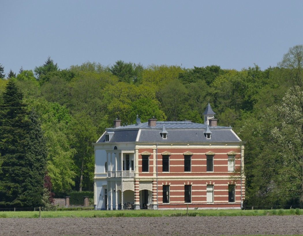 Twee verdiepingen tellend bakstenen en wit huis, bomen op de achtergrond, blauwe lucht.