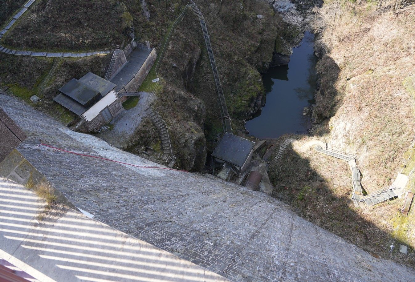 Een steile betonnen damwand kijkt uit over een kleine, donkere waterpoel in een rotsachtige, ruige kloof.