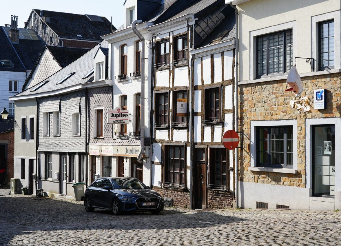 Een donkere auto geparkeerd op een straat met kinderkopjes voor een rij historische gebouwen met vakwerk en stenen gevels.