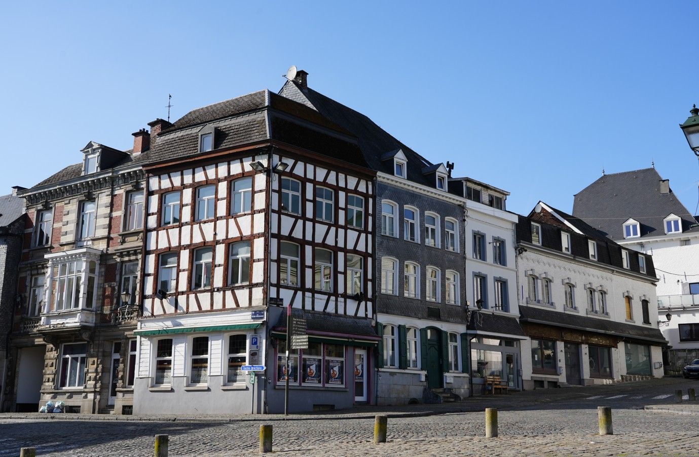 Een straatbeeld van historische Europese vakwerkpanden met kinderkopjes als straatstenen onder een helderblauwe hemel.