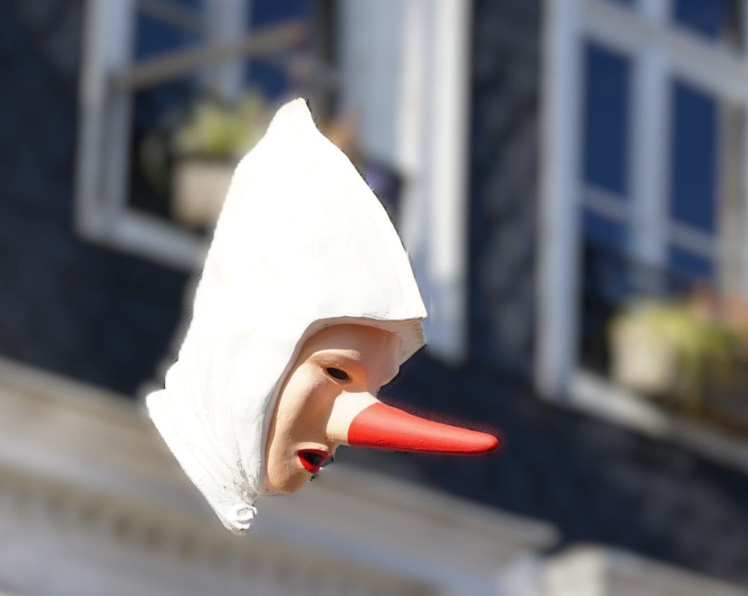 Een zwevend poppenhoofd met een witte, puntige kap en een lange, rood getipte neus.