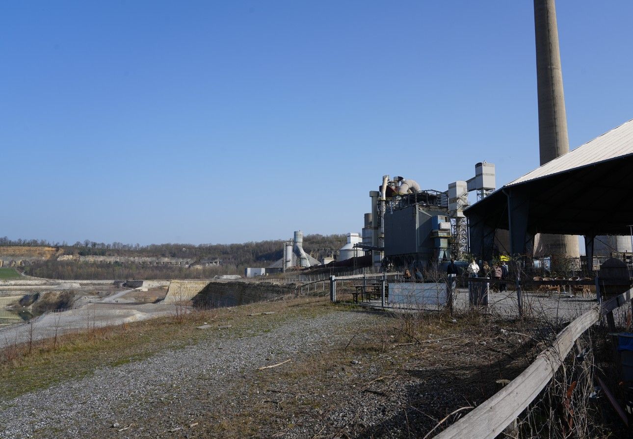 Een industrieel complex met grote schoorstenen en gebouwen die uitkijken over een uitgestrekte, kale steengroeve.