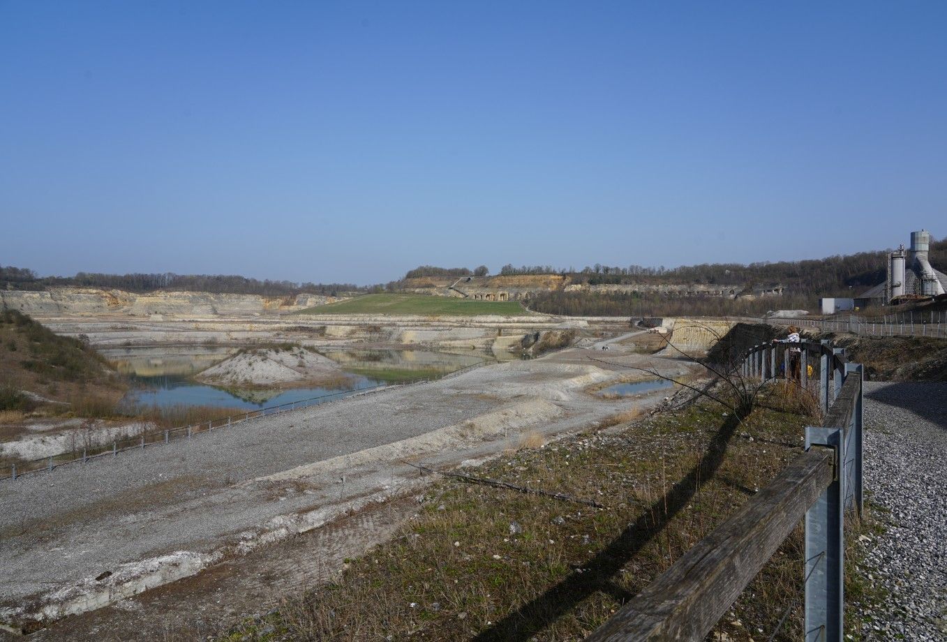 Een breedbeeldopname van een uitgestrekte, gedeeltelijk onder water staande steengroeve onder een helderblauwe hemel.