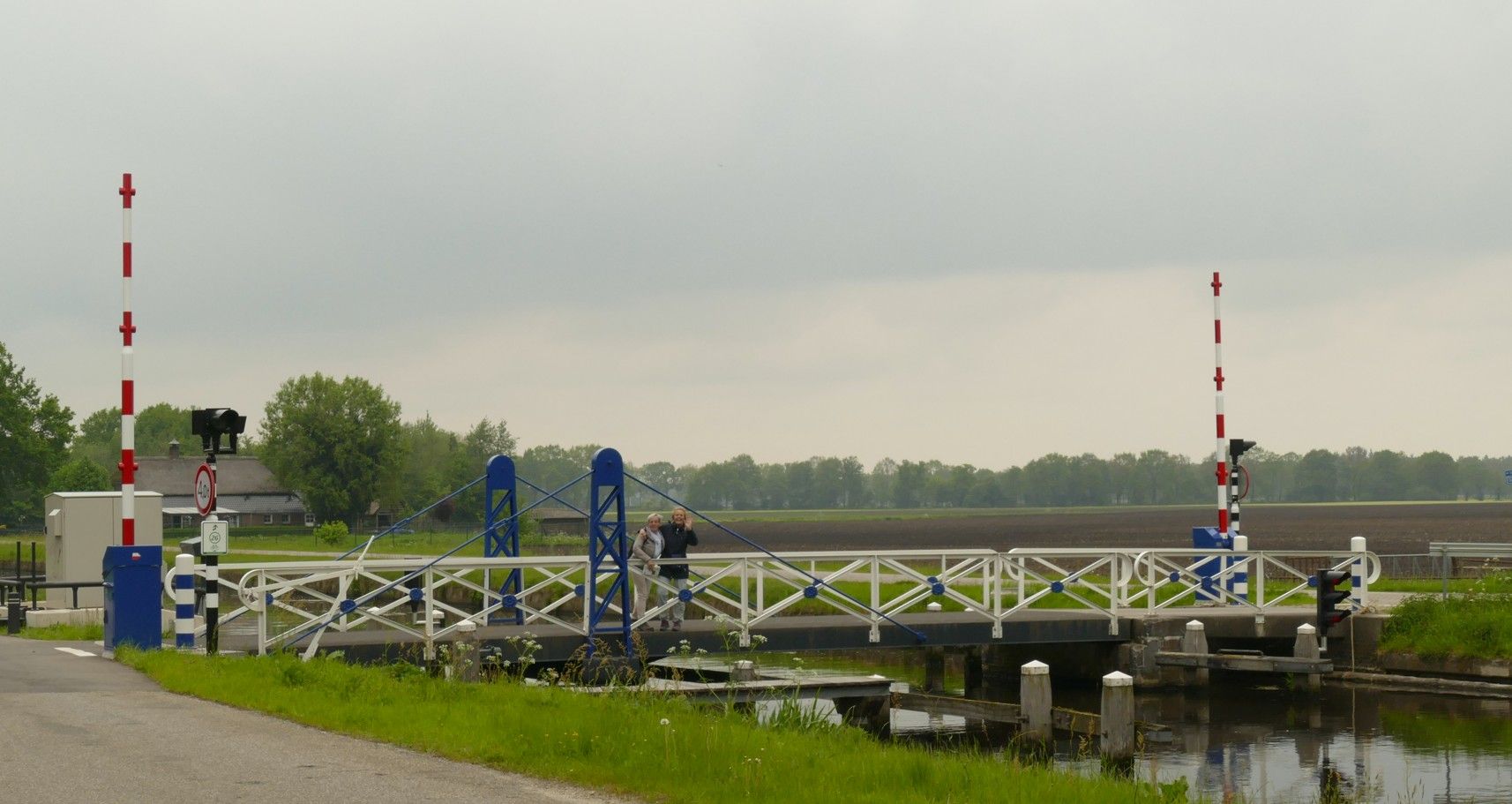 Een ophaalbrug over een kanaal met verhoogde wit-blauwe slagbomen; aan weerszijden staan ​​rood-wit gestreepte palen.