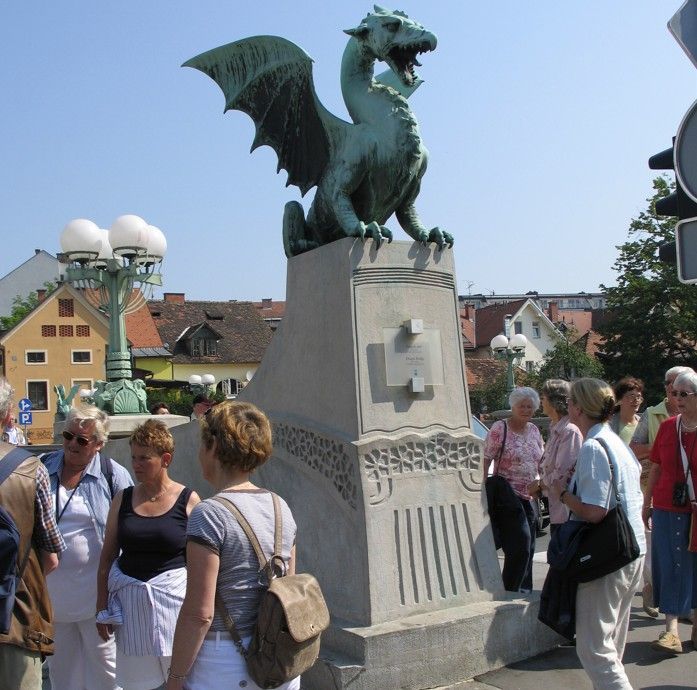 Drakenbeeld op een brug in Ljubljana, Slovenië, met toeristen. De bronzen draak heeft zijn vleugels uitgespreid; een groep mensen staat op de voorgrond.