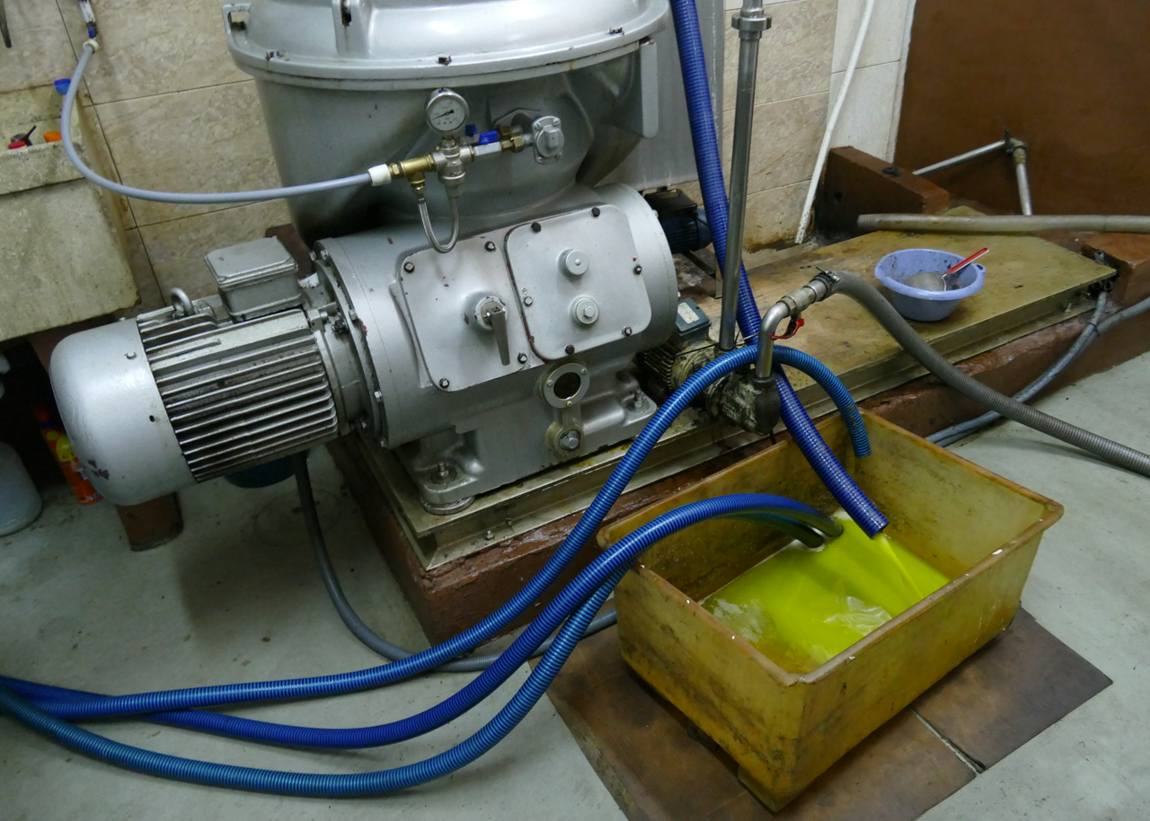 Industriële machine met blauwe slangen die een groenachtige vloeistof in een gele bak spuit.