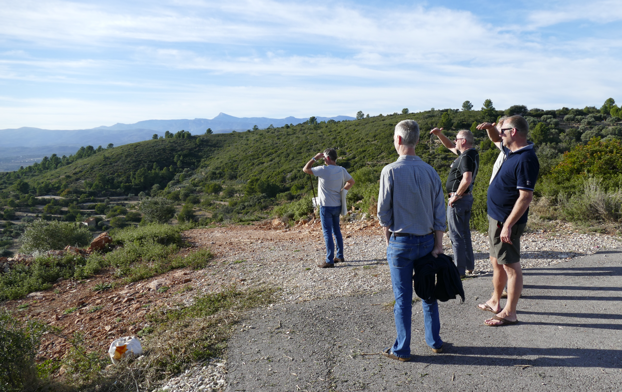 Vier mensen staan ​​op een weg en kijken naar een bergachtig landschap. Het is een zonnige dag.