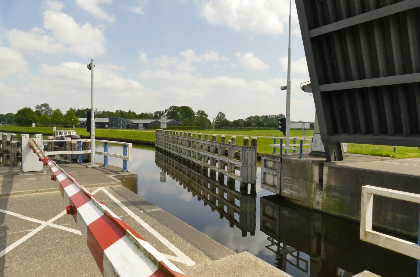 Een ophaalbrug over een kanaal, gedeeltelijk omhoog. Een rood-witte slagboom op de weg. 