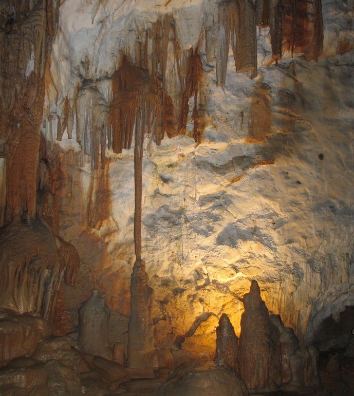 Het interieur van de grot wordt verlicht door warm licht, waardoor stalactieten en stalagmieten op de ruwe rotswanden goed zichtbaar zijn.