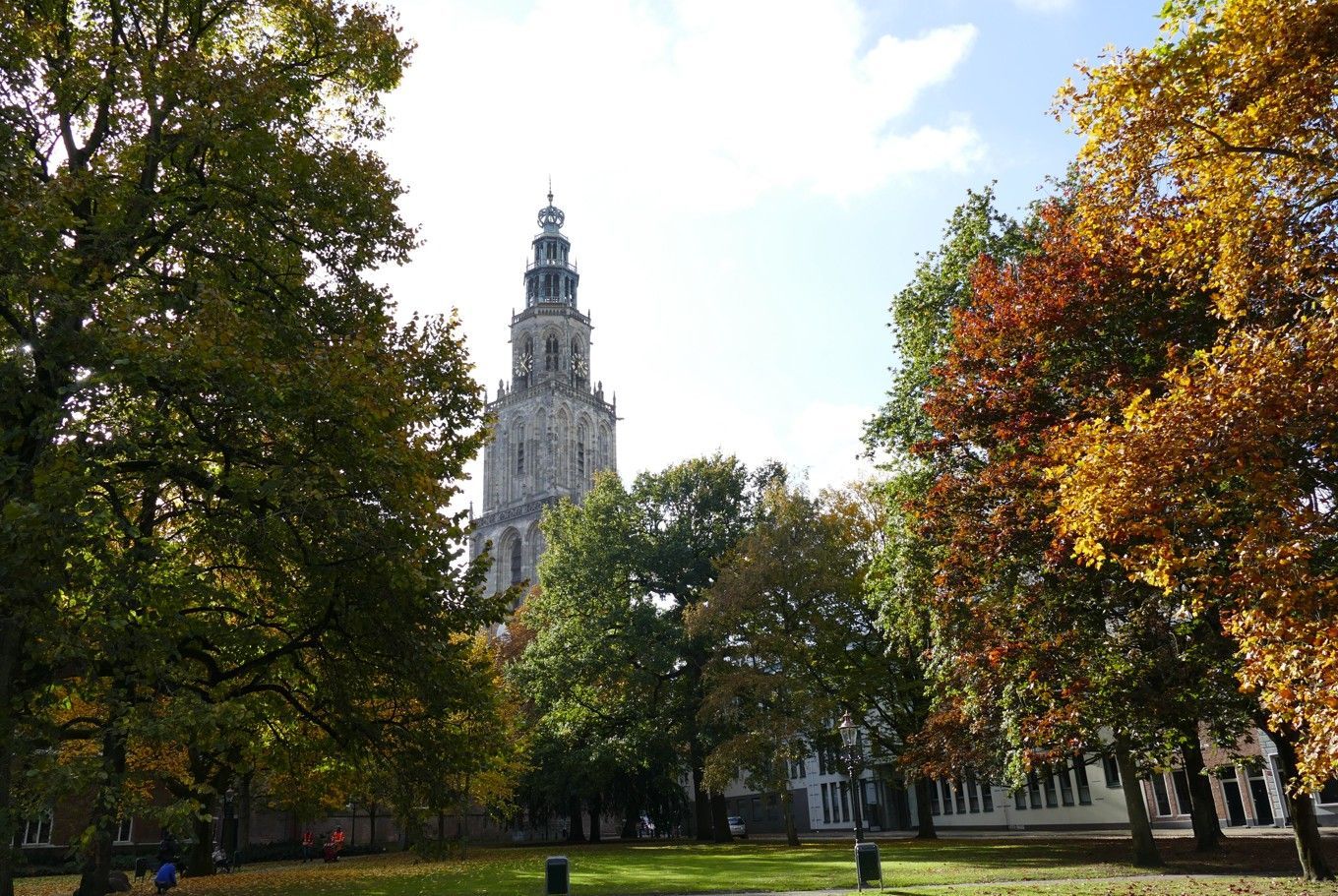 Hoge kerktoren omlijst door herfstbomen met kleurrijke bladeren.
