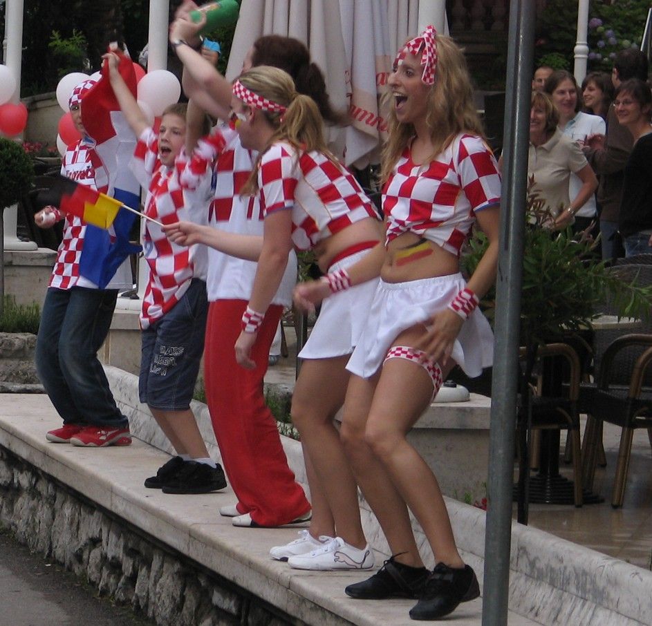Mensen in geruite overhemden en witte rokken vieren feest, zwaaien met vlaggen en juichen.