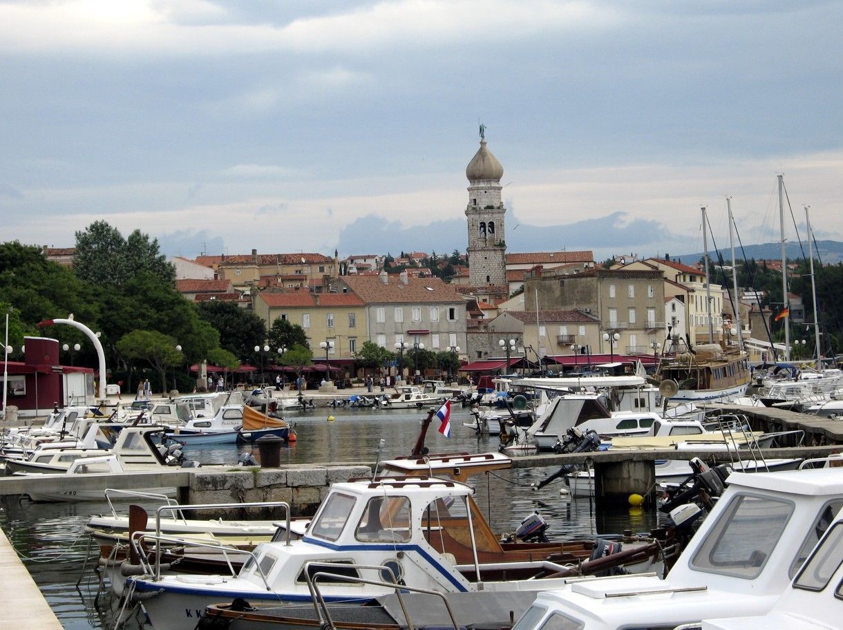 Een haven met boten en een stadje met een hoge kerktoren onder een bewolkte hemel.