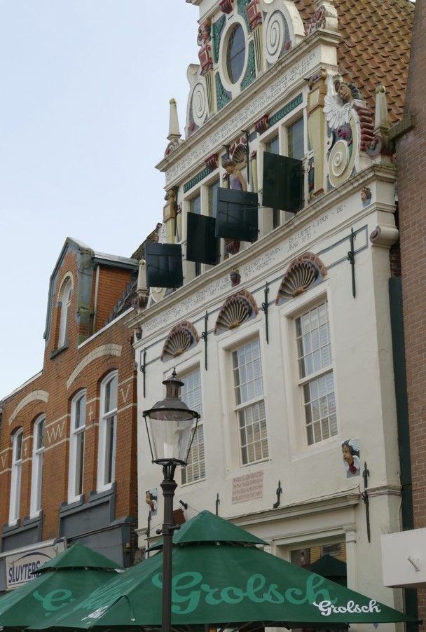 Historische Nederlandse gebouwen met wit-rode gevels, winkelpuien en groene parasols.