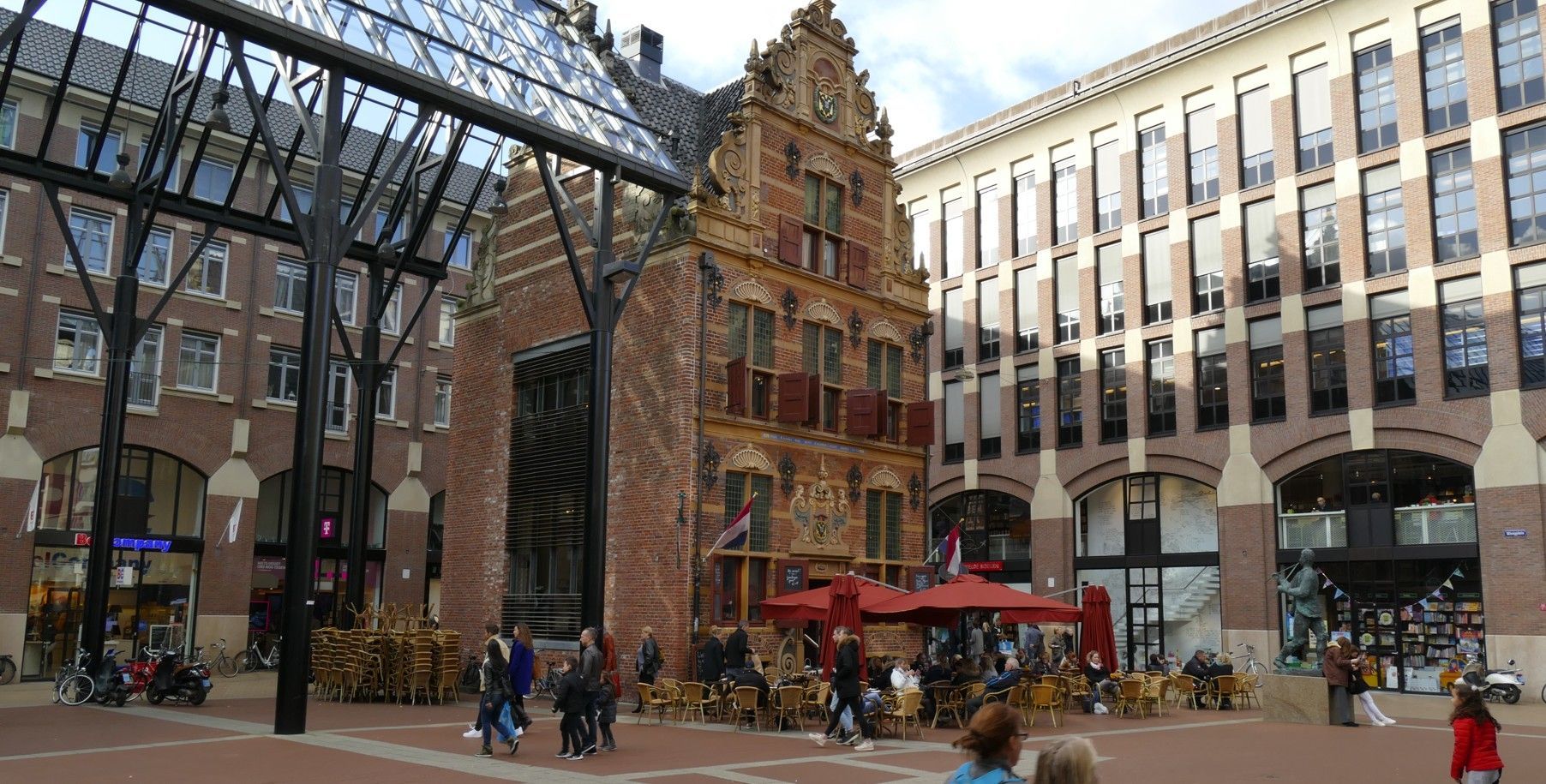 Historisch gebouw met een sierlijke gevel, een binnenplaats vol mensen en omliggende bakstenen gebouwen.