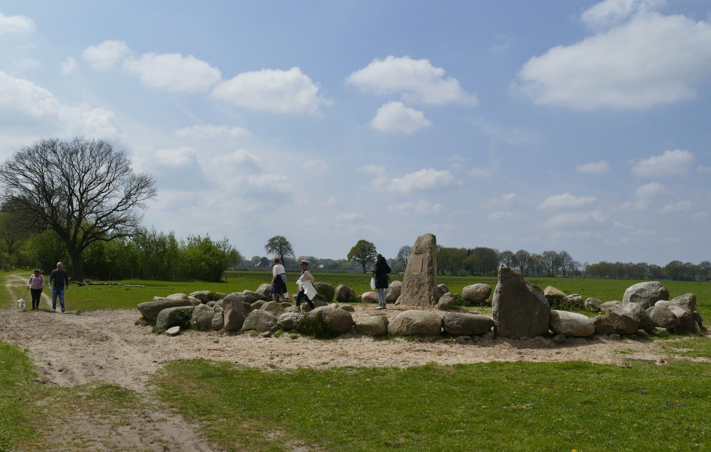 Een op Stonehenge lijkende stenen constructie in een grasveld met mensen in de buurt op een zonnige dag.