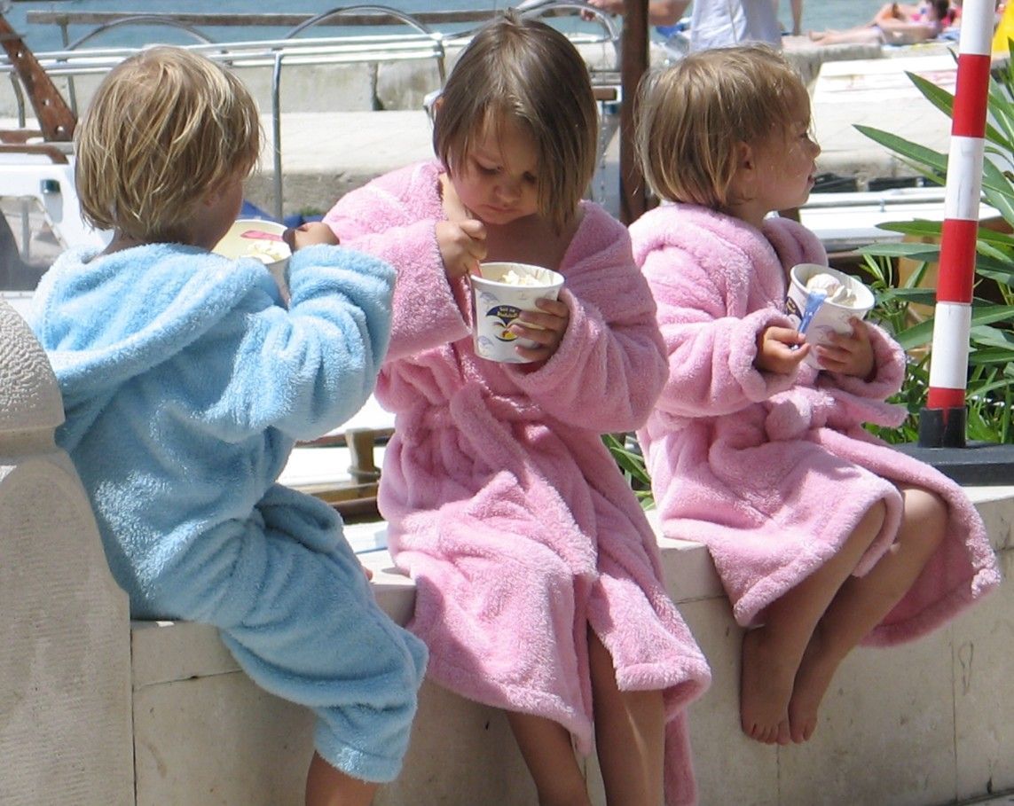 Drie kinderen in badjassen eten buiten ijs. Eén in een blauwe, twee in een roze.