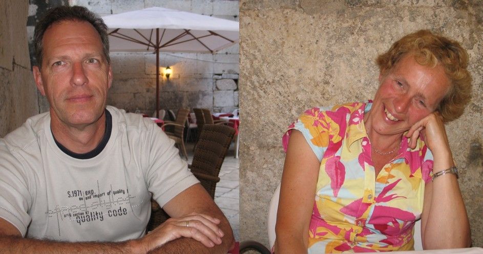 Man in gestreept shirt, vrouw in top met bloemenprint. Beiden glimlachen, in een buitenomgeving met tafels en een stenen muur.