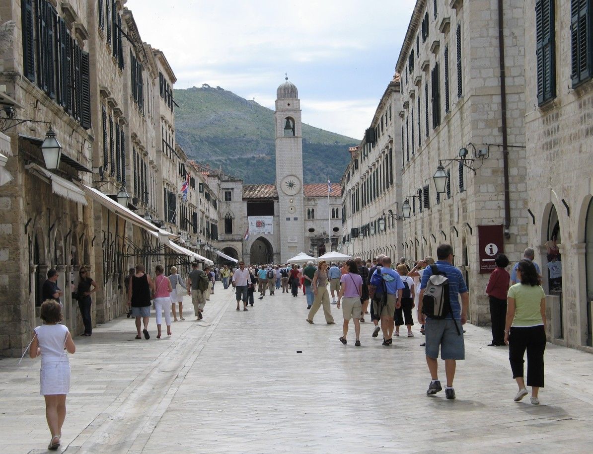 Een straat met kinderkopjes en gebouwen, voetgangers lopen richting een klokkentoren.