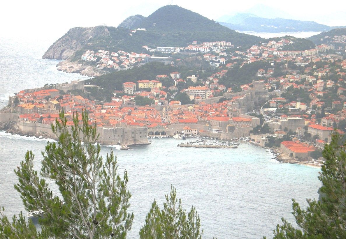 Uitzicht op de kust van Dubrovnik, Kroatië, met gebouwen met rode daken, stenen muren en de omringende bergen en zee.