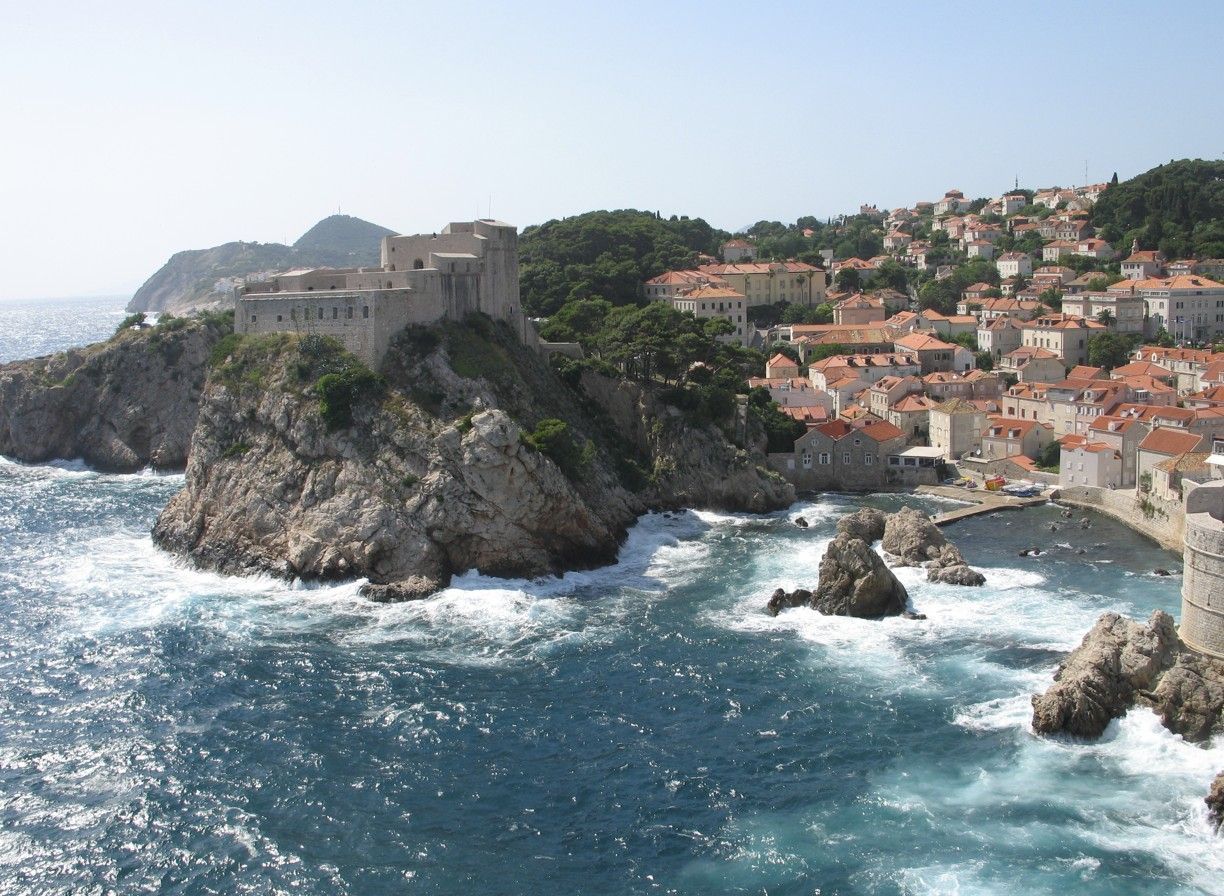 De kuststad Dubrovnik met een fort op rotsachtige kliffen, een blauwe zee en rode pannendaken.