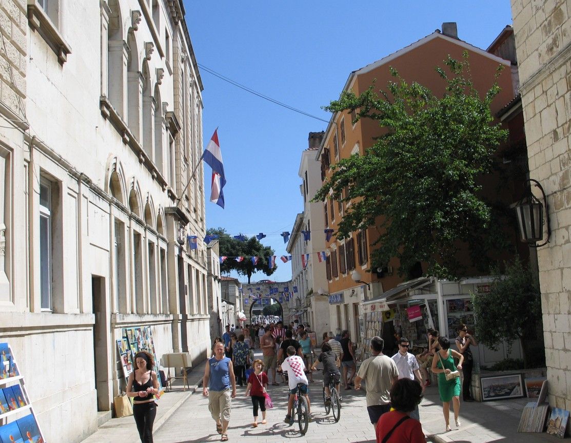 Smalle straat met voetgangers en fietsers. Gebouwen met vlaggen. Zonnige dag.
