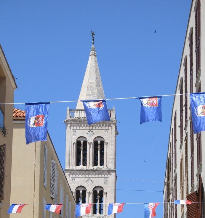Stenen kerktoren met blauwe vlaggen tegen een heldere, blauwe hemel.